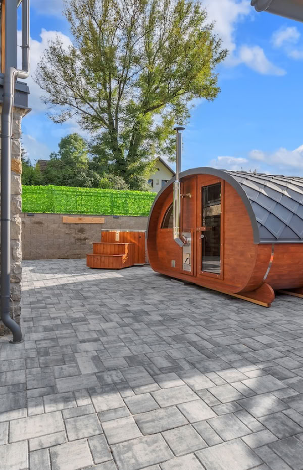 Outdoor patio area with stone paving, a wooden pod structure, two orange deck chairs, and a tree in the background.